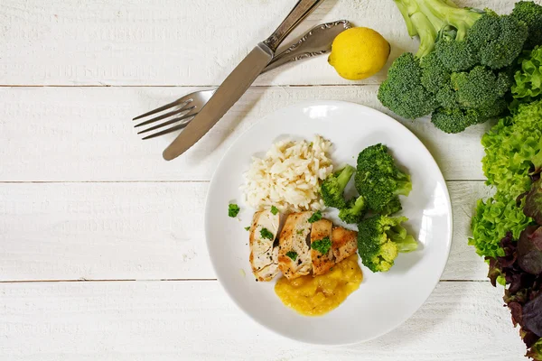 Fried chicken breast fillet with a fruity sauce, broccoli and rice on a white wooden background, top view from above