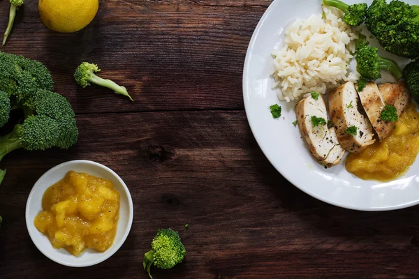 Fried chicken breast fillet with stewed fruit, broccoli and rice  on a rustic dark wooden background, top view from above
