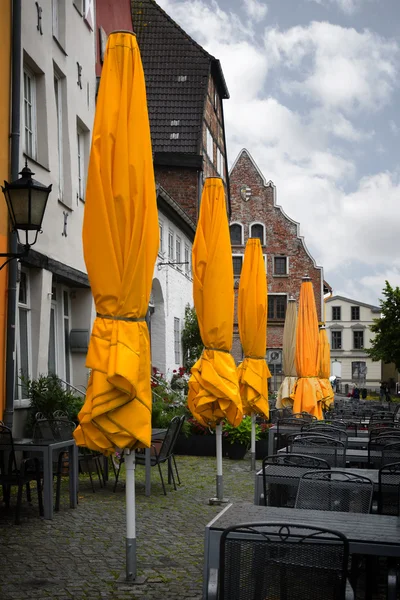 Closed yellow sun umbrellas in a street cafe on a rainy summer day in the old town of Wismar, Germany