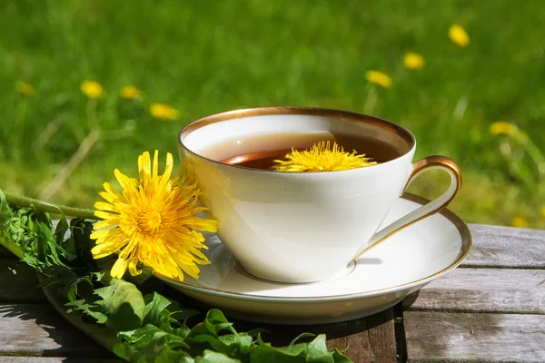 Dandelion tea in a white cup on a wooden table against a blurry meadow