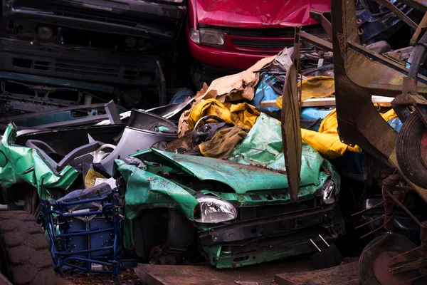 Colors on the junkyard, crushed turquoise scrap car, yellow garbage and a red junk car between the brown metal waste