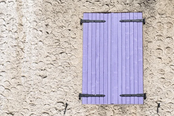 Closed window shutters of purple wood in a rough-plastered wall