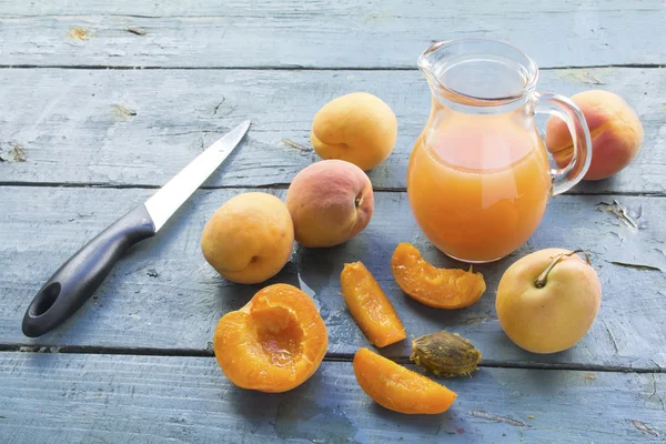 Apricots,  juice in a glass jug and a knife on an old blue wood