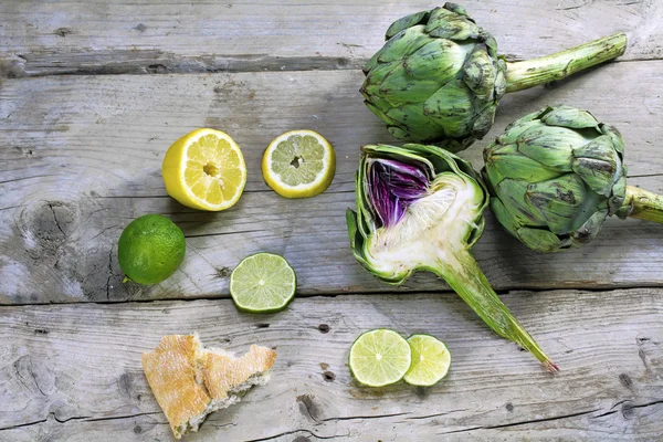 Artichokes whole and halved with lemons, limes and bread on weat