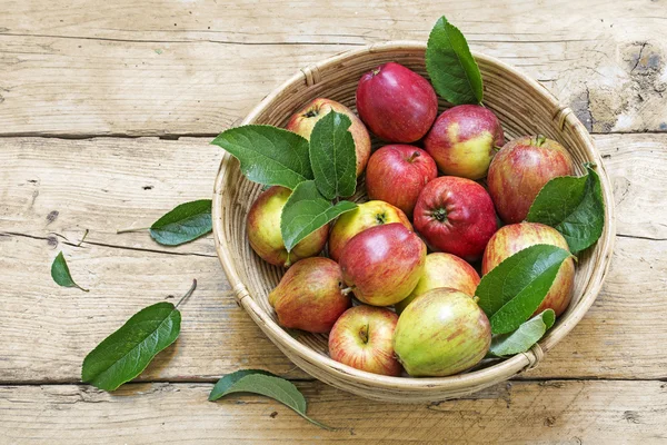Apples and leaves in a basket on a rustic wooden table