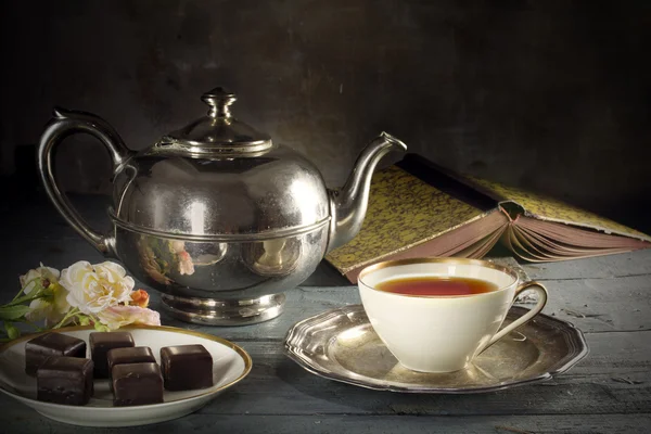 Tea in a porcelain cup, old fashioned silver teapot, chocolate c