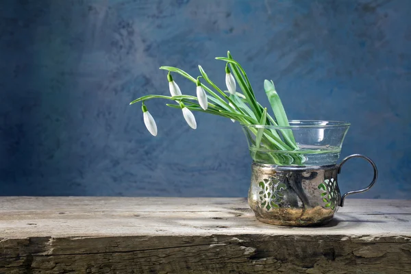 Snowdrops in an old vase of silver and glass on a rustic wooden