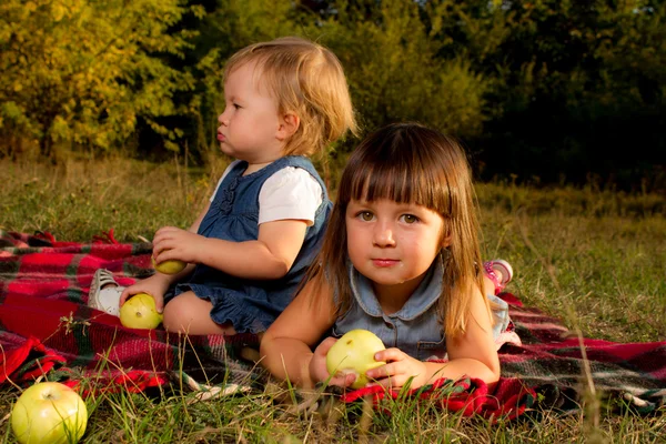 Happy children lying on green grass outdoors in spring park with apples