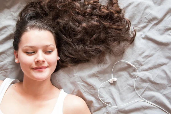 Beautiful young woman laying down on bed with headphones