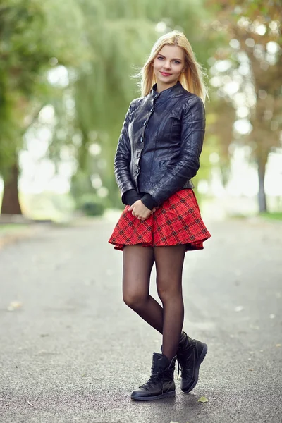 Young trendy dressed blonde woman demonstrate her weekend outfit posing on park path shallow depth of field