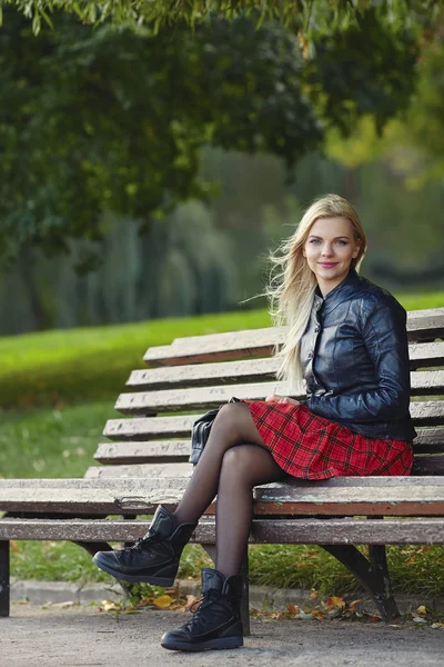 Closeup outdoors portrait of young adorable blonde woman sitting on the park bench  in windy weather conditions with green blurry background