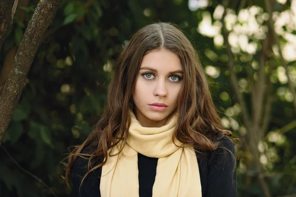 Closeup outdoor portrait of young cute brunette woman with wavy long hair looking into camera posing against forest park background