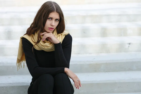 Closeup portrait of young beautiful brunette woman with wavy long hair stares into camera sitting on the concrete stairs