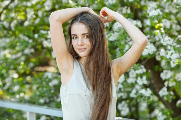 Portrait of the young beautiful brunette woman in pastel dress with extra long hair with raised arms again blossoming tree outdoors