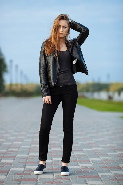 Happy young beautiful woman in black leather jacket black jeans slip-on posing for model tests in the summer park