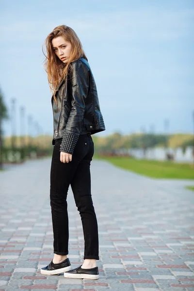 Happy young beautiful woman in black leather jacket black jeans slip-on posing for model tests in the summer park