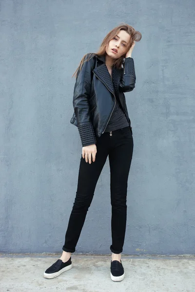 Happy young beautiful woman in black leather jacket black jeans slip-on posing for model tests against textured wall