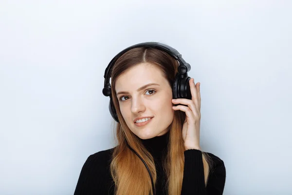Portrait of happy smiling young beautiful woman in black sweater big dj headphones posing against white studio background