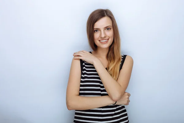 Portrait of happy young beautiful woman in striped shirt hugging herself posing for model tests against white studio background