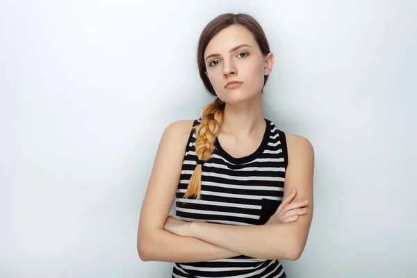 Portrait of serious naughty young beautiful woman in striped shirt posing with crossed arms for model tests against studio background