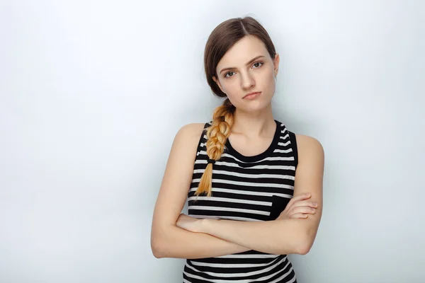 Portrait of serious naughty young beautiful woman in striped shirt posing with crossed arms for model tests against studio background