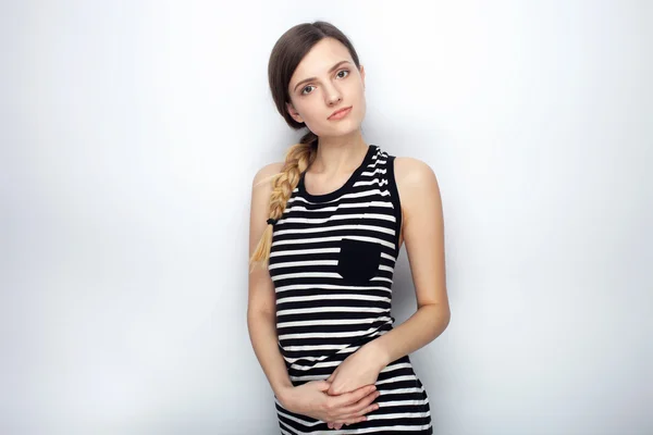Portrait of cute young beautiful woman in striped shirt questioningly looking into camera posing for model tests against studio background