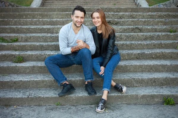 Portrait of young love couple dressed casual trendy style sitting together on steps of a concrete stairway warm season outdoor