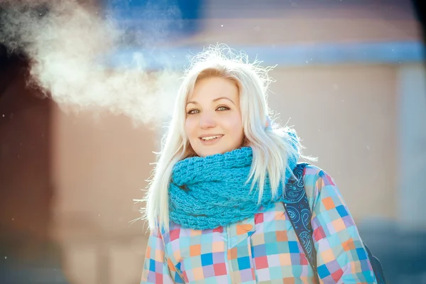 Joyful naughty blonde woman in bright jacket and scarf exhales in winter city outdoors