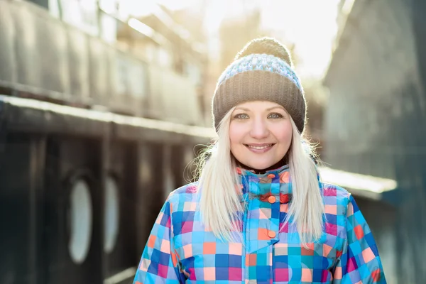 Smiling naughty blonde woman in bright jacket and hat with pompom against the background aboard the ships sunny winter outdoors