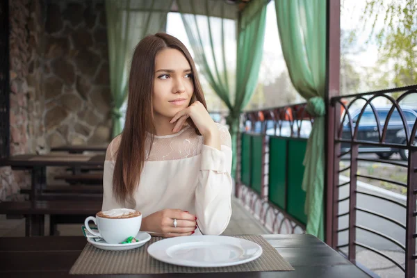 Young beautiful brunette woman waiting at the cafe terrace with a cappuccino cup