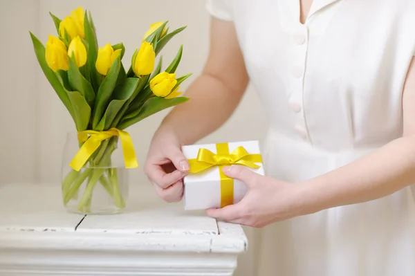 Beautiful woman with a gift and fresh yellow tulips.