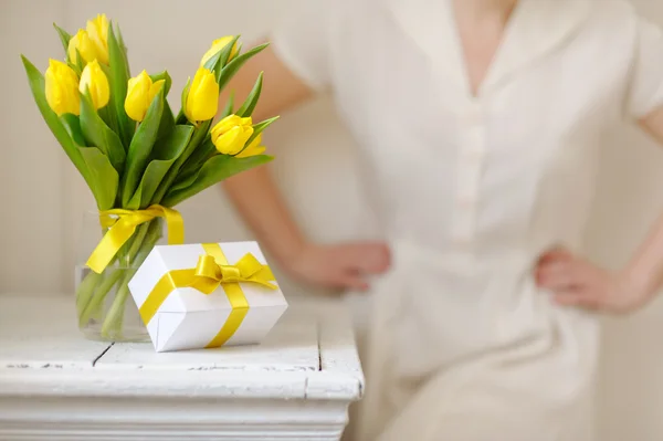 Beautiful woman with a gift and fresh yellow tulips.