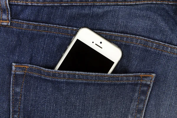 Part of mobile white cellphone in the back pocket of blue denim