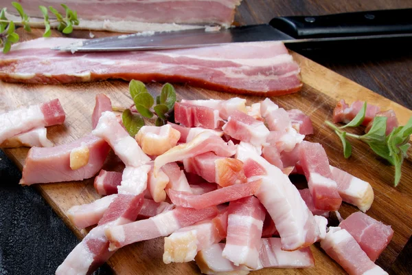Fresh raw homemade bacon sliced on cubes on wooden table with green herb