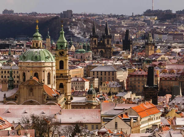 Amazing St. Nicolas church during winter day after heavy snow storm with snow cover at roofs. Sunny winter day in Old town district, Prague, Czech republic.