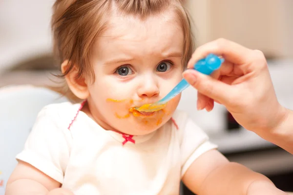 Little girl feeding from a spoon on blue chair.