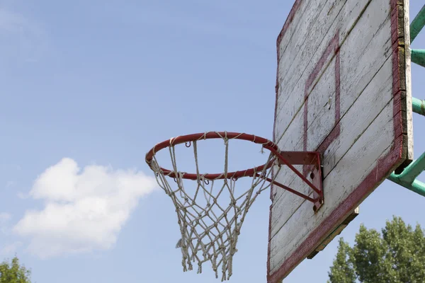 Basketball board with a net. Old, wooden planks. Painted. Located on a background of blue sky with clouds. Sport games in the yard. Side view.