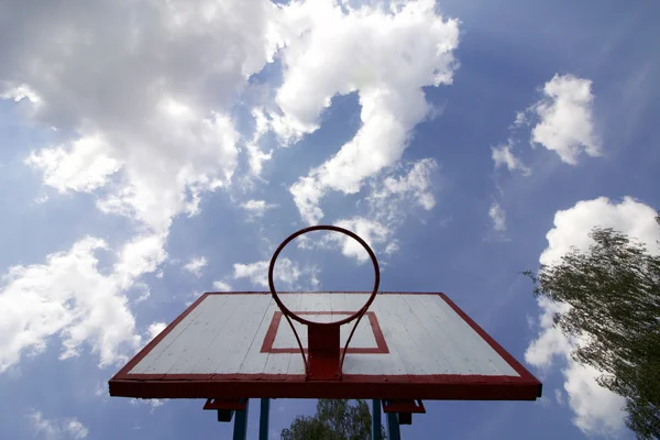 Basketball board without net. Old, wooden planks. Painted. Located on a background of blue sky with clouds. Sport games in the yard. View from under the ring.