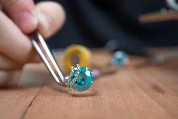 Desktop jeweler. jeweler holding tweezers silver ring with blue stone