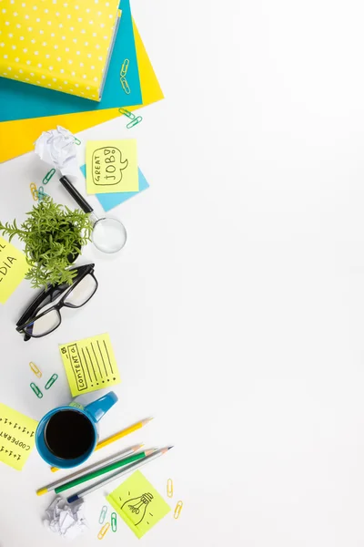 Office table desk with green supplies, blank note pad, cup, pen, glasses, crumpled paper, magnifying glass, flower on white background. Top view