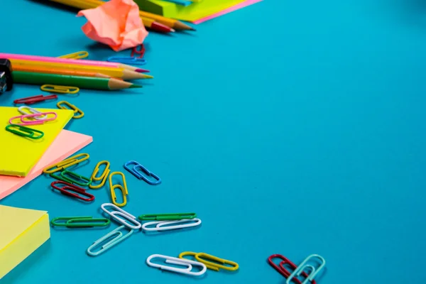 Office table desk with set of colorful supplies, white blank note pad, cup, pen, pc, crumpled paper, flower on blue background. Top view and copy space for text