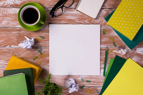 Office table desk with supplies, white blank note pad, cup, pen, pc, crumpled paper, flower on wooden background. Top view