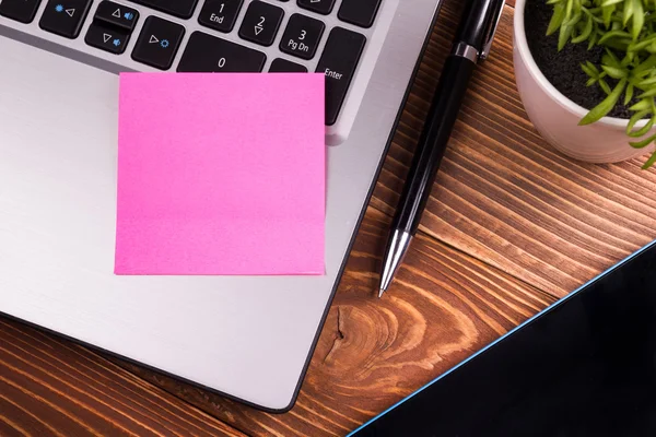 Office table desk with supplies, white blank note pad, cup, pen, pc, crumpled paper, flower on wooden background. Top view