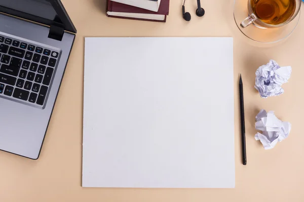 Office table desk with set of colorful supplies, white blank note pad, cup, pen, pc, crumpled paper, flower on beige background. Top view and copy space for text