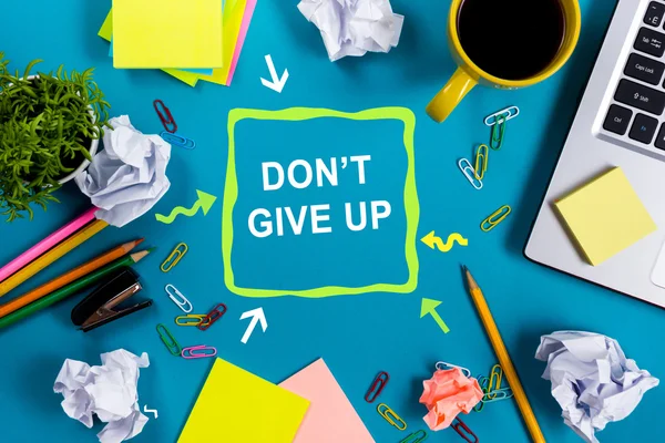 Dont give up. Office table desk with supplies, white blank note pad, cup, pen, pc, crumpled paper, flower on blue background. Top view