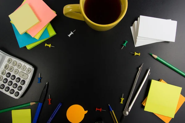 Office table desk top view with set of colorful supplies, white blank note pad, cup, pen, pc, crumpled paper, flower on blue background. Top view and copy space for text