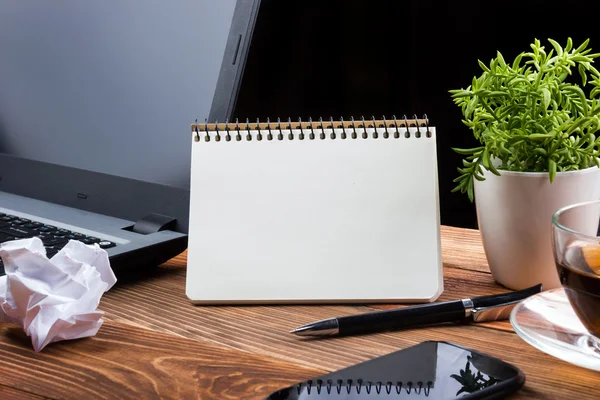 Office table desk with supplies, white blank note pad, cup, pen, pc, crumpled paper, flower on wooden background. Top view