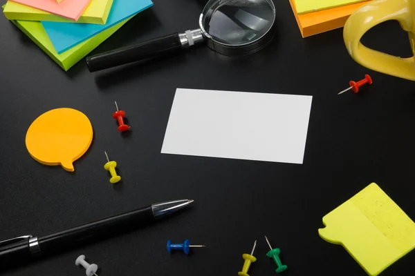 White blank business card. Office table desk with set of colorful supplies, cup, pen, pencils, flower, notes, cards on black board desk table background. Top view and copy space for ad text