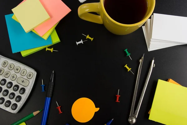 Office table desk top view with set of colorful supplies, white blank note pad, cup, pen, pc, crumpled paper, flower on blue background. Top view and copy space for text