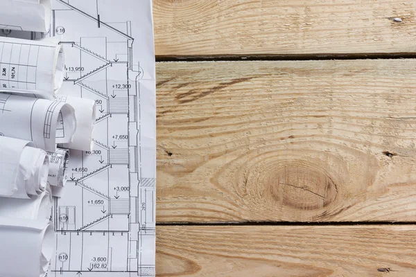Architectural project, blueprints, blueprint rolls near checkered blank paper with pen on vintage wooden background. Construction concept. Architect workplace top view. Copy space